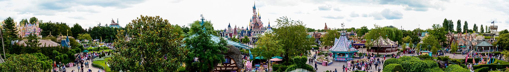 Panoramic view across Fantasyland at Disneyland Paris, with colourful attractions, gardens and distant castle turrets